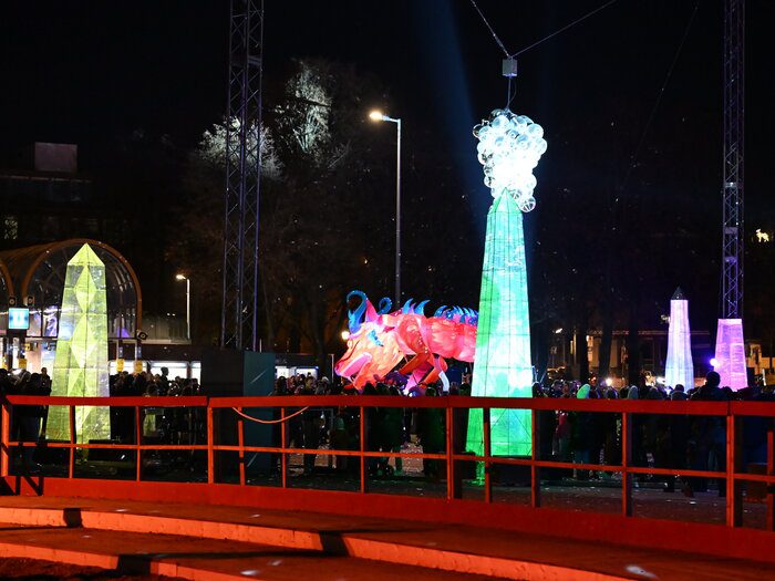 Leuchtender Drache neben grünem Glasobelisken mit Lichterkugeln